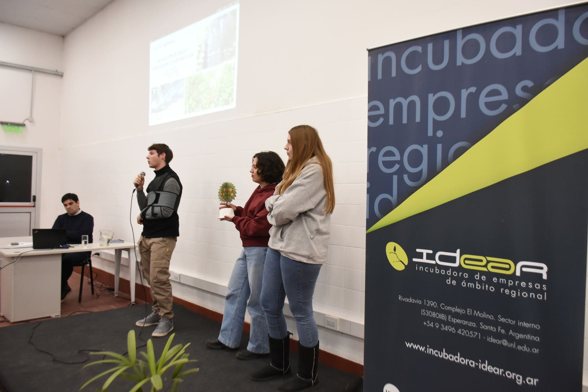 Emprendedoras presentando su proyecto junto al banner de la Incubadora IDEAR
